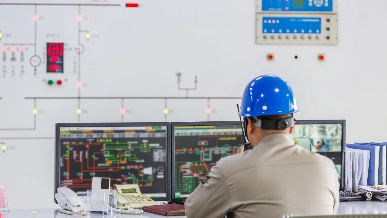 Operador acompanha sistemas de uma instalação industrial em uma sala de controle