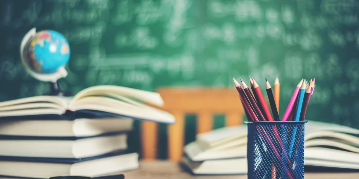 Books, pencils and globe in front of a green board