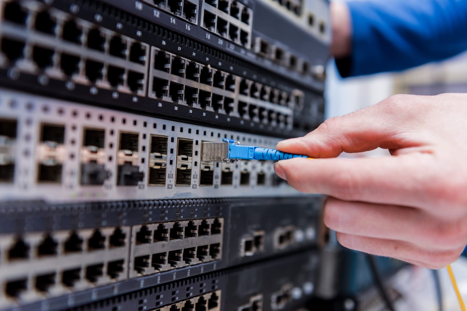 Mão conectando um cabo de rede a um switch em um rack de equipamentos corporativos