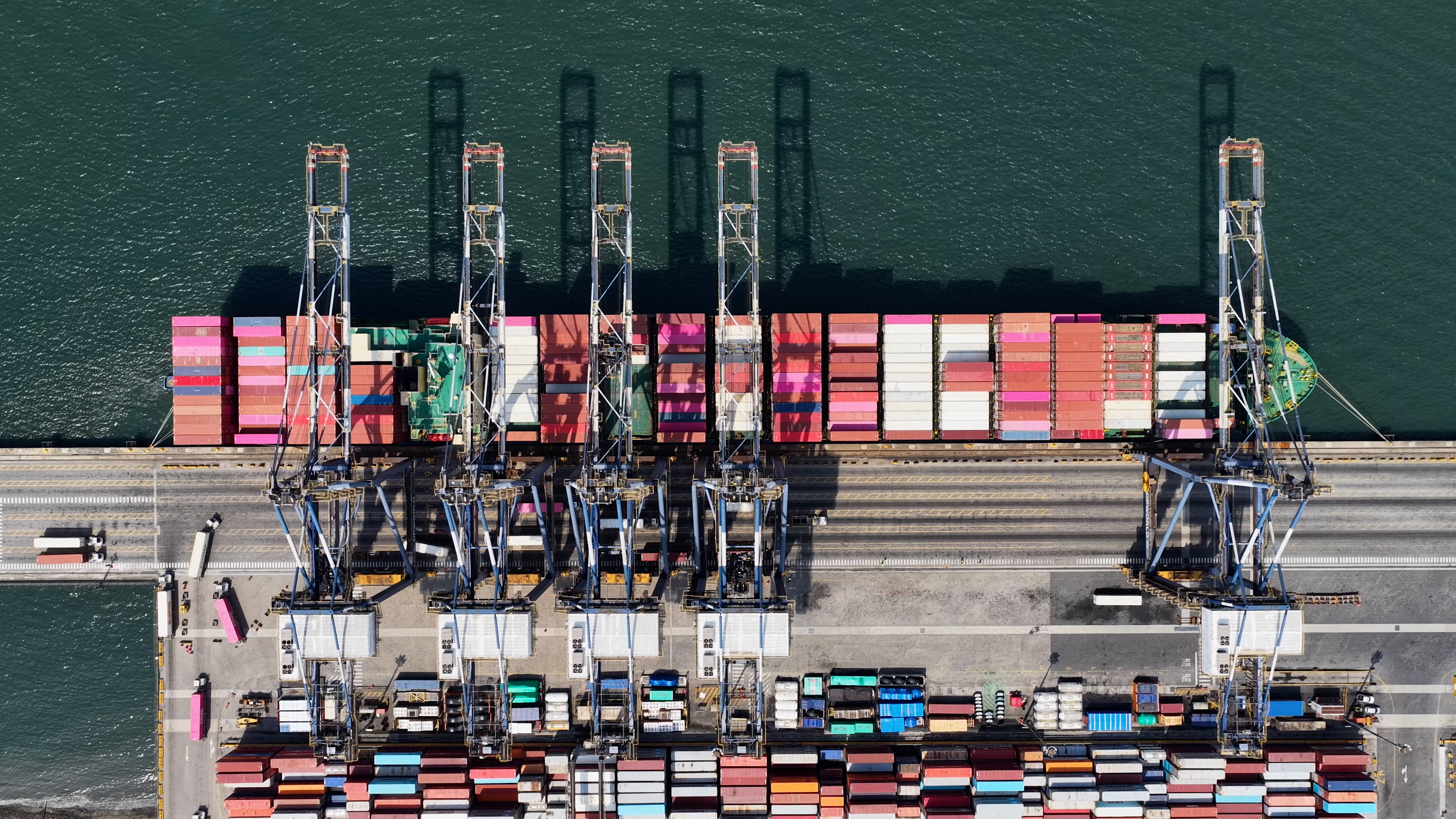 Vista aérea de navio cargueiro atracado entre guindastes e contêineres em terminal portuário